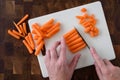 WomanÃ¢â¬â¢s hands chopping baby carrots, white cutting board on wood butcher block
